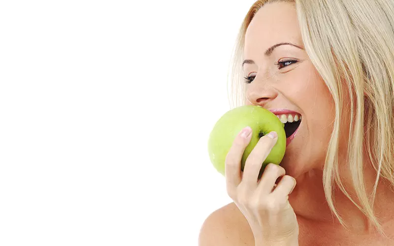 Frau beißt genussvoll und fröhlich in einen Apfel